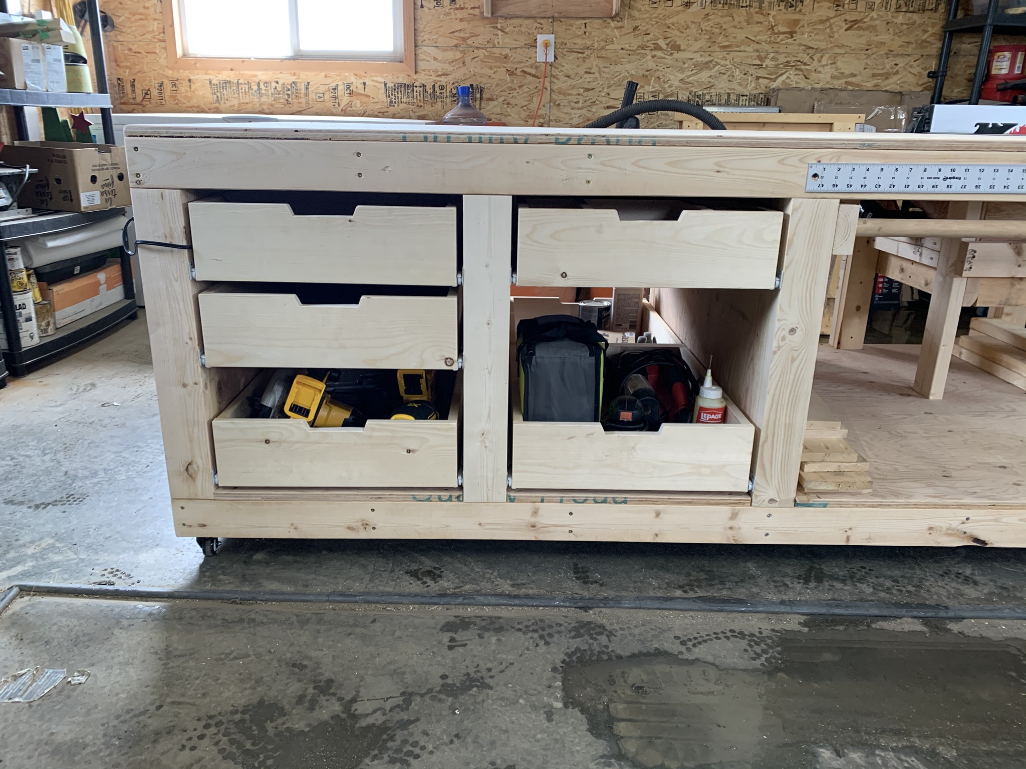 Cordless drills, tool bags and wood glue stored in the open drawers of a garage workbench